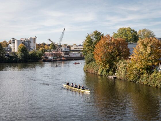 Eine Gruppe von Menschen, die in einem Boot einen Fluss befahren, umgeben von Natur und industriellen Gebieten.
