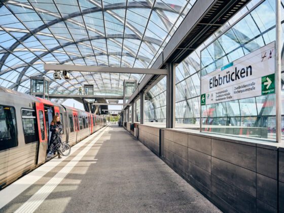 Moderne U-Bahnstation mit einem Glasdach, an dem eine Person mit einem Fahrrad aus einem Zug aussteigt.