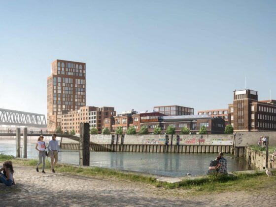 Urbane Flussufer-Szene mit mehreren Personen, die am Wasser entlang spazieren, einem Hund, der spielt, und Industriegebäuden im Hintergrund. Der Himmel ist klar und blau.