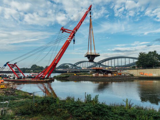 Ansicht vom anderen Ufer: Ein Kran transportiert ein Brückenteil.
